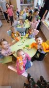Dzieci siedzą przy stolikach i pokazują wykonane z rolek i papieru wiewiórki. 